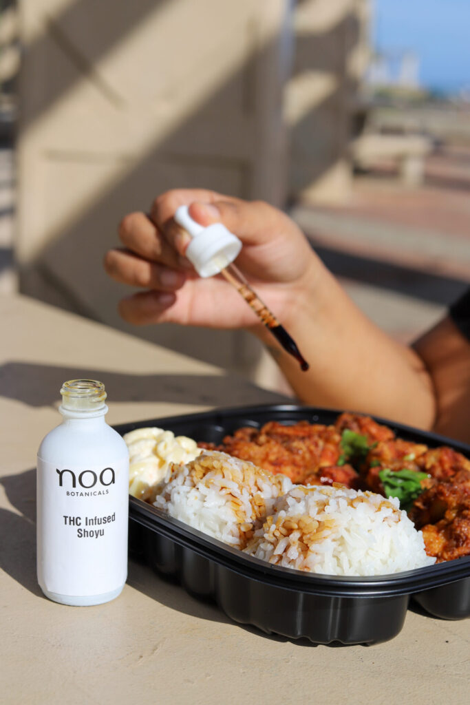 A person adding THC-Cannabis infused shoyu from a small bottle to a plate of rice and curry, outdoors.