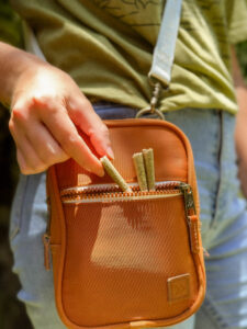 A person places two of Hawaii's dog walker pre-rolls into the front pocket of a small, orange crossbody bag.