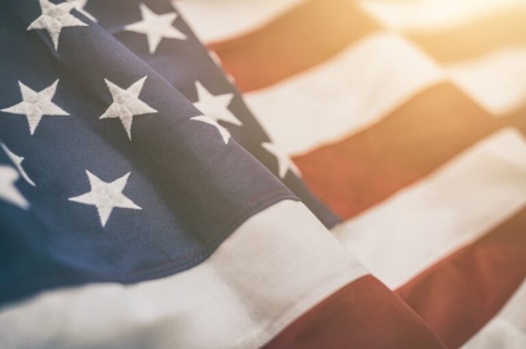 Close-up of a United States flag waving, with stars on a blue field and red and white stripes, symbolizing unity. Sunlight highlights the fabric texture akin to the strength of our communities supported by discount programs.